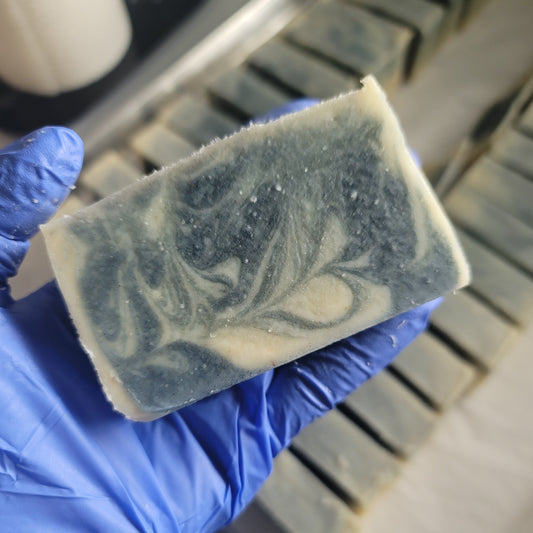 Bar of soap with a blue marbled design held by a gloved hand, with more bars in the background.